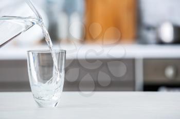 Pouring of fresh water into glass on table in kitchen�