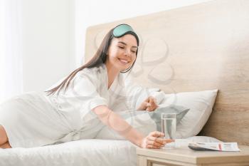 Morning of beautiful young woman taking glass of water from bedside table�