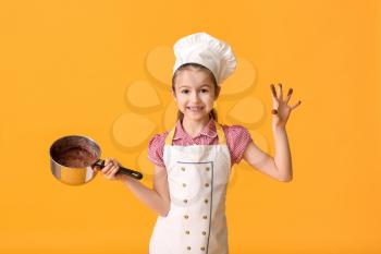 Little housewife with melted chocolate in saucepan on color background�