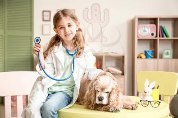 Cute little girl dressed as doctor playing with dog at home�