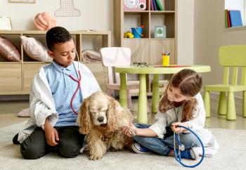 Cute little children dressed as doctors playing with dog at home�