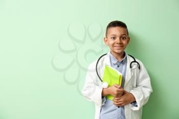 Cute little African-American doctor on color background�