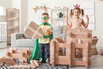 Little children in costumes playing with take-apart house at home�