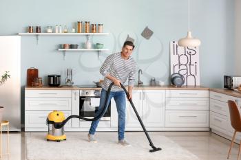 Young man hoovering floor in kitchen�