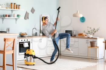 Young man listening to music while hoovering floor in kitchen�