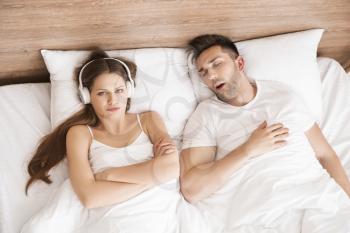 Young irritated woman in bed with snoring husband at home�