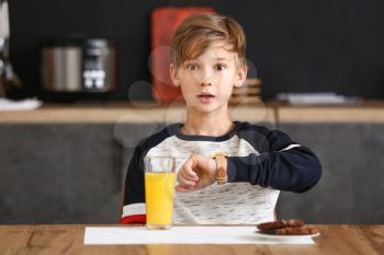 Surprised little boy looking at his watch while having breakfast in kitchen�