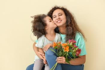 Little African-American girl with her mother and bouquet on color background�