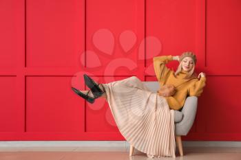 Young woman in warm sweater sitting near color wall�