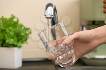 Woman filling glass with fresh water from kitchen faucet�