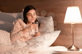 Young woman drinking water in bedroom at night�