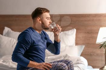 Young man drinking water in bedroom at night�