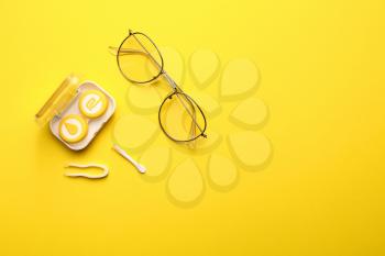 Container with contact lenses and glasses on color background�