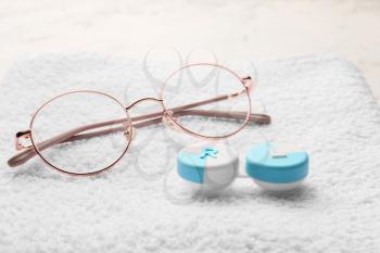 Container with contact lenses and glasses on towel�