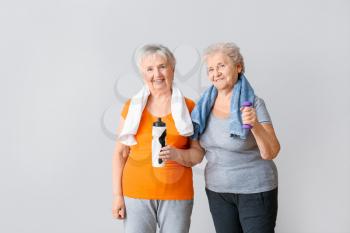 Happy elderly women with bottle of water and dumbbell on light background�