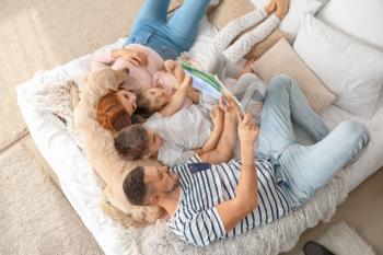Happy family with dog reading book in bedroom at home�