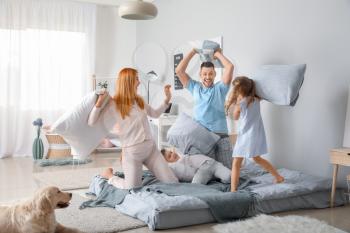 Happy family fighting on pillows in bedroom at home�