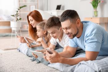 Happy family with modern devices in bedroom at home�