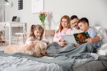 Happy family with dog reading book in bedroom at home�