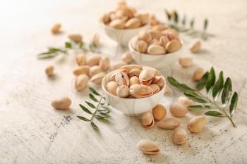 Bowls with tasty pistachio nuts on light background�