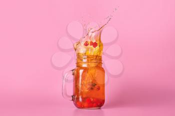 Mason jar of cold tea with splashes on color background�