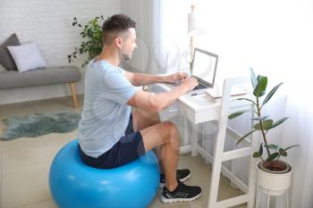 Man sitting on fitness ball while working at home�