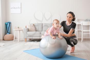 Young sporty mother and her baby doing exercises with fitball at home�