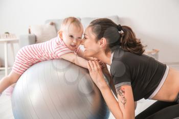 Young sporty mother and her baby doing exercises with fitball at home�