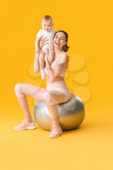 Young sporty mother and her baby doing exercises with fitball on color background�