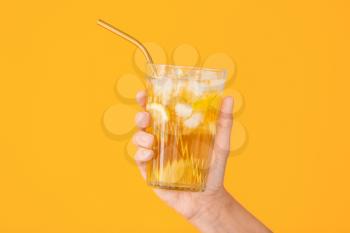 Female hand with cold tea in glass on color background�