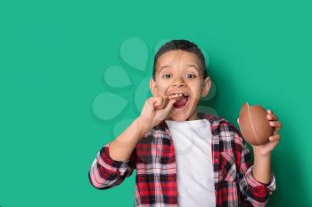 Cute African-American boy with sweet chocolate egg on color background�