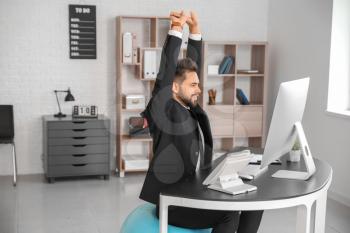 Businessman sitting on fitness ball while working in office�