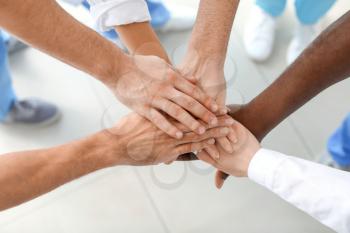 Group of doctors putting hands together in clinic. Unity concept�