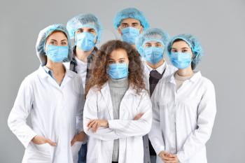 Group of doctors with protective masks on grey background. Concept of epidemic�