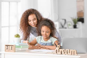 Little African-American girl with her mother doing homework in room�