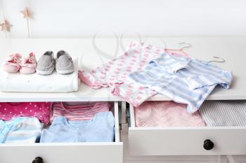 Chest of drawers with clean baby clothes and booties in room�