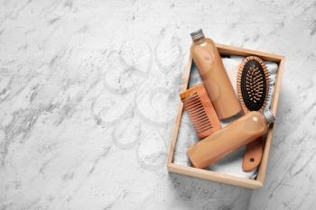 Box with shampoo, comb, towel and brush on light background�