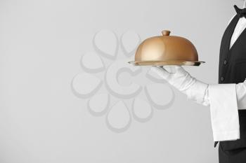 Male waiter with tray and cloche on grey background�