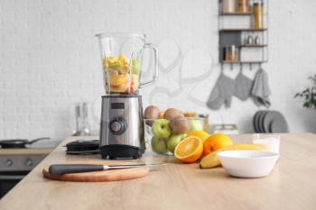 Modern blender with fresh fruits and cutting board on table in kitchen�