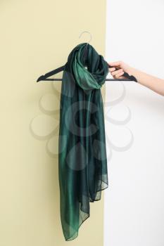 Female hand holding hanger with beautiful scarf on light background�