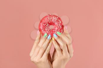 Hands of young woman with beautiful manicure and donut on color background�