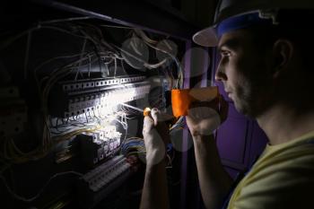 Male electrician with flashlight repairing distribution board�