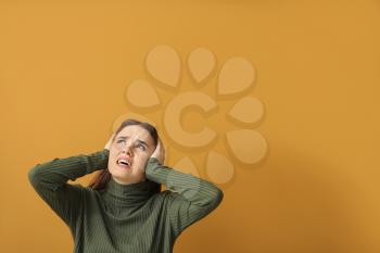 Young woman suffering from loud noise on color background�