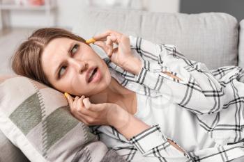 Young woman with ear plugs suffering from loud noise at home�