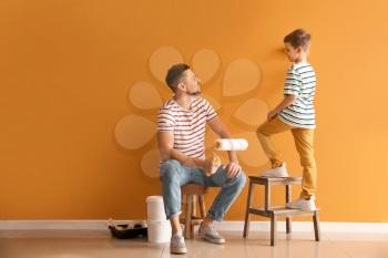 Little son helping his father to paint wall at home�