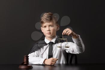 Portrait of little judge sitting at table against dark background�