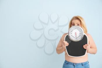 Troubled overweight woman with scales on color background. Weight loss concept�
