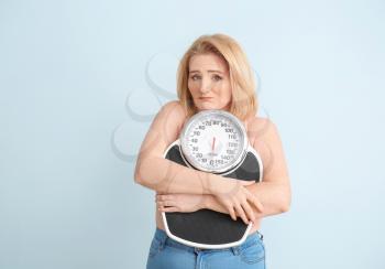Sad overweight woman with scales on color background. Weight loss concept�