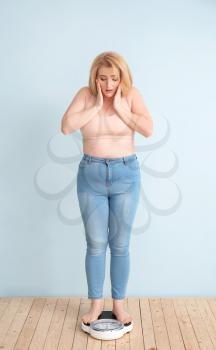 Troubled overweight woman with scales on color background. Weight loss concept�