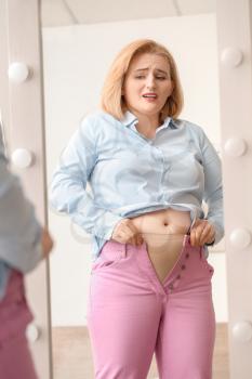 Troubled overweight woman in tight clothes near mirror at home�